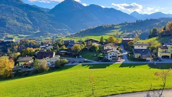 Malerische Landschaft mit weiten grünen Feldern und Häusern vor imposanter Bergkulisse.