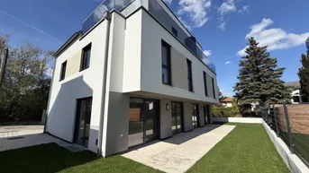 Moderne Neubaufassade mit großen Fenstern, kleiner Rasenfläche und gepflastertem Zugangsbereich.