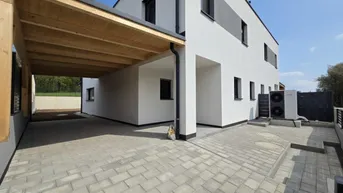 Moderne Doppelhaushälfte mit Carport und gepflasterter Einfahrt unter blauem Himmel.