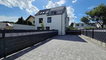 Modernes Einfamilienhaus mit gepflasterter Einfahrt und klarem Himmel an einem sonnigen Tag.