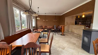 Geräumiger Gastraum mit Holztischen, Bänken und Fliesenboden, ideal für ein Restaurant oder Café.