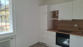 Moderne Einbauküche mit weißen Schränken, Holzakzenten und Blick auf einen historischen Innenhof.