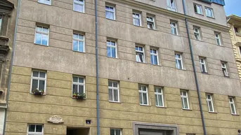 Mehrstöckiges Wohngebäude mit beiger Fassade, blauen Dachelementen und parkenden Autos davor.