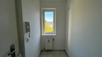 Heller Flur mit weißen Fliesen, einer Gegensprechanlage und einem Fenster mit Ausblick.