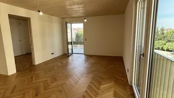 Heller Wohnraum mit Fischgrätparkettboden, Holzbalkendecke und Zugang zu einem Balkon.