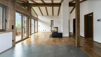 Heller Wohnbereich mit Holzbalken, Kamin und großen Fensterfronten zum Balkon.