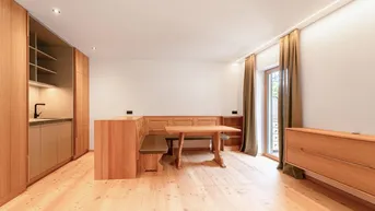 Helles Wohn- und Esszimmer mit Holzboden, integrierter Küchenzeile und traditioneller Sitzecke.