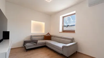 Helles Wohnzimmer mit modernem Ecksofa, Holzboden und Blick auf die Berge.