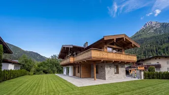 Neues Chalet im traditionellen Stil mit Holz- und Steinfassade, Balkonen und großem Garten vor alpiner Bergkulisse.