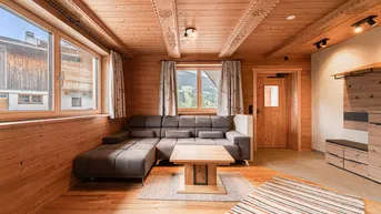 Gemütliches Wohnzimmer im alpinen Stil mit Holzwänden, geschnitzter Holzdecke und bequemer Eckcouch.