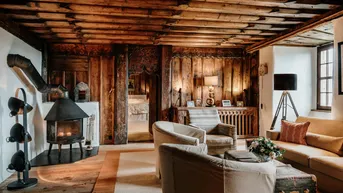 Gemütliches Wohnzimmer mit Holzbalkendecke, Kaminofen und traditioneller Einrichtung.