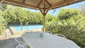 Überdachter Essbereich im Freien mit Blick auf den Pool und den grünen Garten.