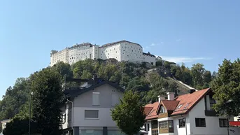 Blick auf eine historische Festung auf einem Hügel mit Wohnhäusern im Vordergrund unter blauem Himmel.