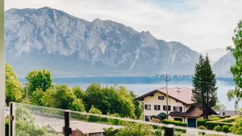 Panoramablick auf den See und die umliegenden Berge mit einem charmanten Haus im Vordergrund.