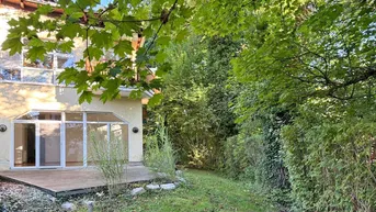Außenansicht des Hauses mit Holzterrasse und umgebendem Gartenbereich unter sonnigem Himmel.