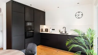 Moderne schwarze Einbauküche mit integrierten Geräten und hellem Holzboden.