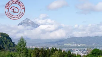 Panoramablick auf eine majestätische Berglandschaft mit Wolken und einer darunter liegenden Stadt.