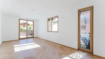 Heller Raum mit Fischgrätparkett, großen Fenstern und Zugang zu einem französischen Balkon.