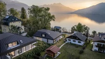 Luftaufnahme von Häusern am Seeufer mit Bergen im Hintergrund bei Sonnenuntergang.
