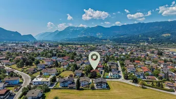 Luftaufnahme einer Wohngegend mit Häusern, grünen Feldern und majestätischen Bergen im Hintergrund.