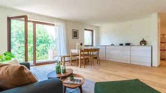 Helles Wohn- und Esszimmer mit Holzboden, Zugang zum Balkon und Blick ins Grüne.