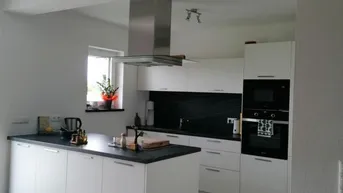Moderne Küche mit weißer Front, dunkler Arbeitsplatte und integrierten Geräten.