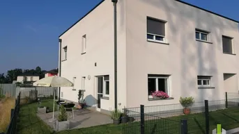 Modernes Haus mit heller Fassade, kleiner Terrasse und Gartenbereich im Sommer.