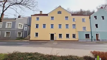 Vorderansicht eines gelben Mehrfamilienhauses an einer Straße mit weiteren Gebäuden.