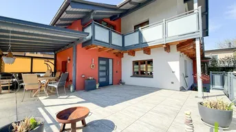 Große, sonnige Terrasse mit überdachtem Sitzbereich und modernem Balkon am Haus.