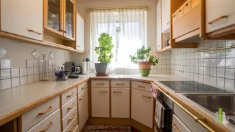 Helle Küche mit weißen Schränken, Holzdetails, Induktionskochfeld und Blick nach draußen.