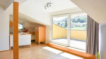 Heller Wohn- und Essbereich mit Holzboden, Dachschrägen und Zugang zu einem sonnigen Balkon.
