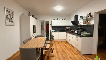 Geräumige Küche mit Essbereich, modernen weißen Schränken, dunkler Arbeitsplatte und Holzboden.