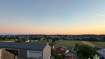 Weitläufiger Blick über die Landschaft und eine Stadt bei Sonnenuntergang mit Bergen am Horizont.