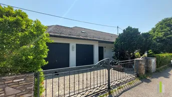 Einfamilienhaus mit Doppelgarage und gepflegter Auffahrt, umgeben von grünen Büschen unter blauem Himmel.