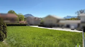 Grüne Rasenfläche mit gepflegter Hecke und weitem Blick auf die Berge unter blauem Himmel.