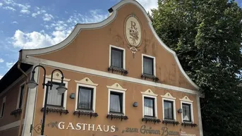 Historisches Gasthaus mit traditioneller Fassade und grünen Akzenten unter blauem Himmel.