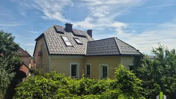 Historisches Gebäude mit gelber Fassade, Satteldach und installierten Solarpaneelen unter blauem Himmel.