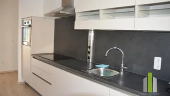 Moderne Einbauküche mit hellen Schränken, dunkler Arbeitsplatte und integrierten Geräten.