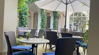Gemütlicher Innenhof mit Sitzgelegenheiten und Sonnenschirm, umgeben von begrünten Fassaden und Kletterpflanzen.