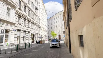 Helle Straße in einer europäischen Stadt mit historischen Gebäuden und einem geparkten Auto.