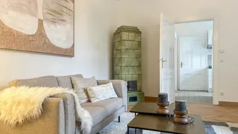 Helles Wohnzimmer mit traditionellem Kachelofen, modernem Sofa und Fischgrätparkettboden.