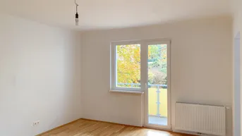 Heller Raum mit Parkettboden, großem Fenster und direktem Zugang zum Balkon.