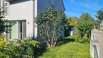 Seitenansicht des Hauses mit gepflegtem Rasen und Sträuchern unter blauem Himmel.