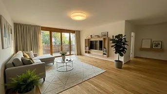 Helles Wohnzimmer mit Holzboden, gemütlichem Sofa und Zugang zu einem Balkon.