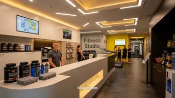 Moderner Empfangsbereich eines Fitnessstudios mit Theke, Regalen und Trainingsgeräten im Hintergrund.