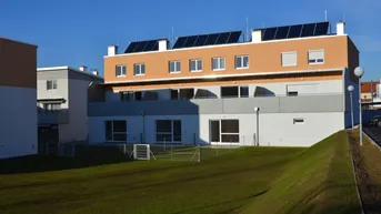 Moderne Wohngebäude mit Photovoltaikanlagen auf dem Dach und einer großen Grünfläche davor.