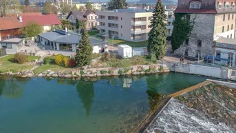 Modernes Wohngebäude am Flussufer mit Blick auf die umliegende Landschaft und historische Bauten.