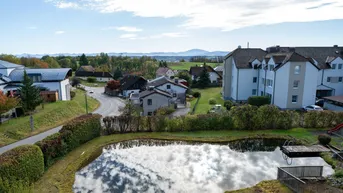 Weitläufiger Blick über die ländliche Umgebung mit einem Teich und Bergen im Hintergrund.