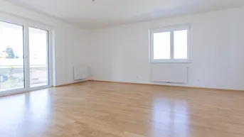 Helles, leeres Zimmer mit Parkettboden und Zugang zu einem sonnigen Balkon.