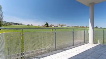 Heller Balkon mit Fliesenboden, modernem Geländer und weitem Blick über grüne Felder.